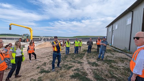 A group of Dane County Board Supervisors stands outside at manure digester site while listening to a speaker explain the process