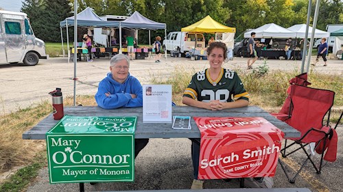 Sarah Smith and Mary O'Connor sit at a picnic table adorned with signs and flyers