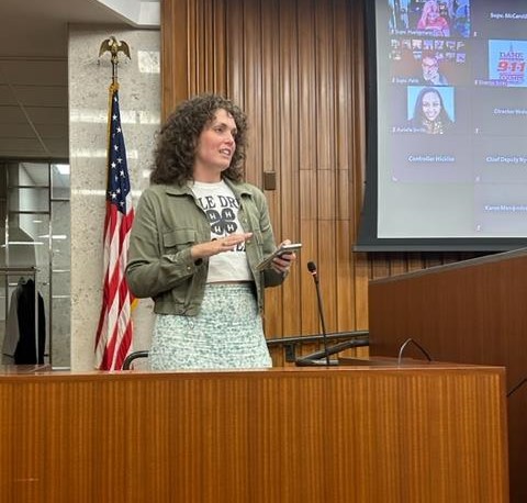 Sarah Smith stands at the podium at the front of the County Board room speaking